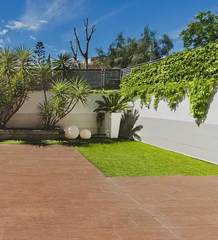 An outdoor fitness studio courtyard with grass, paved areas, white walls, and tropical plants under blue sky