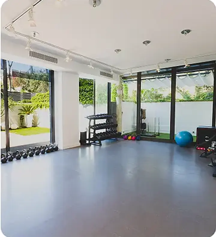 A fitness studio with dark blue flooring, large windows, dumbbells, an exercise ball, and various gym equipment