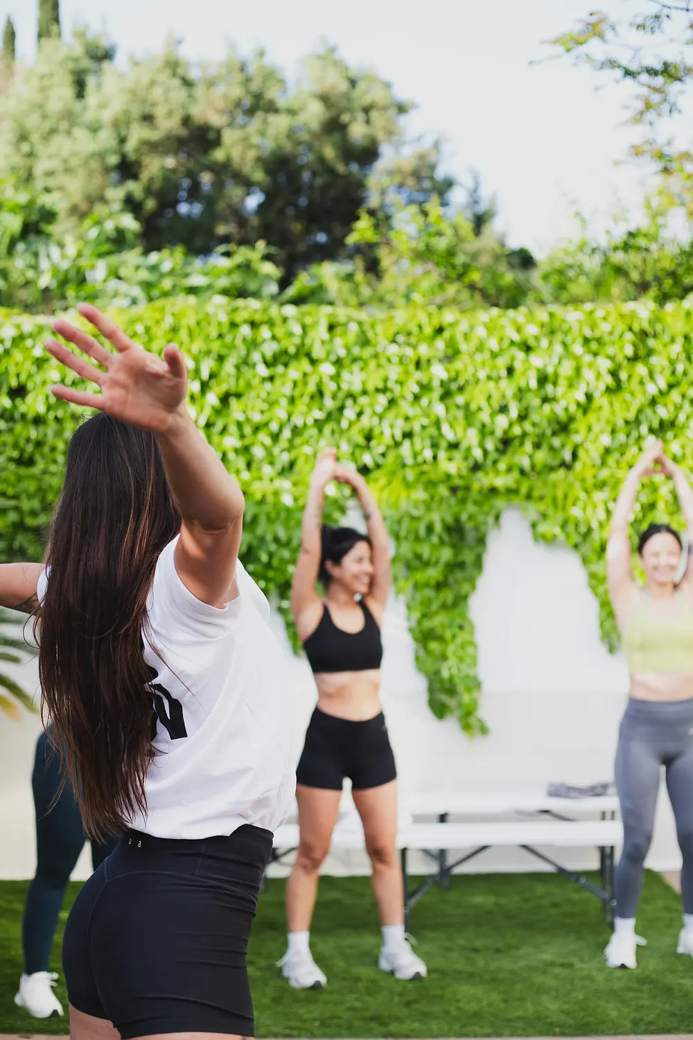 An instructor leading a group stretch exercise during an outdoor fitness class on grass