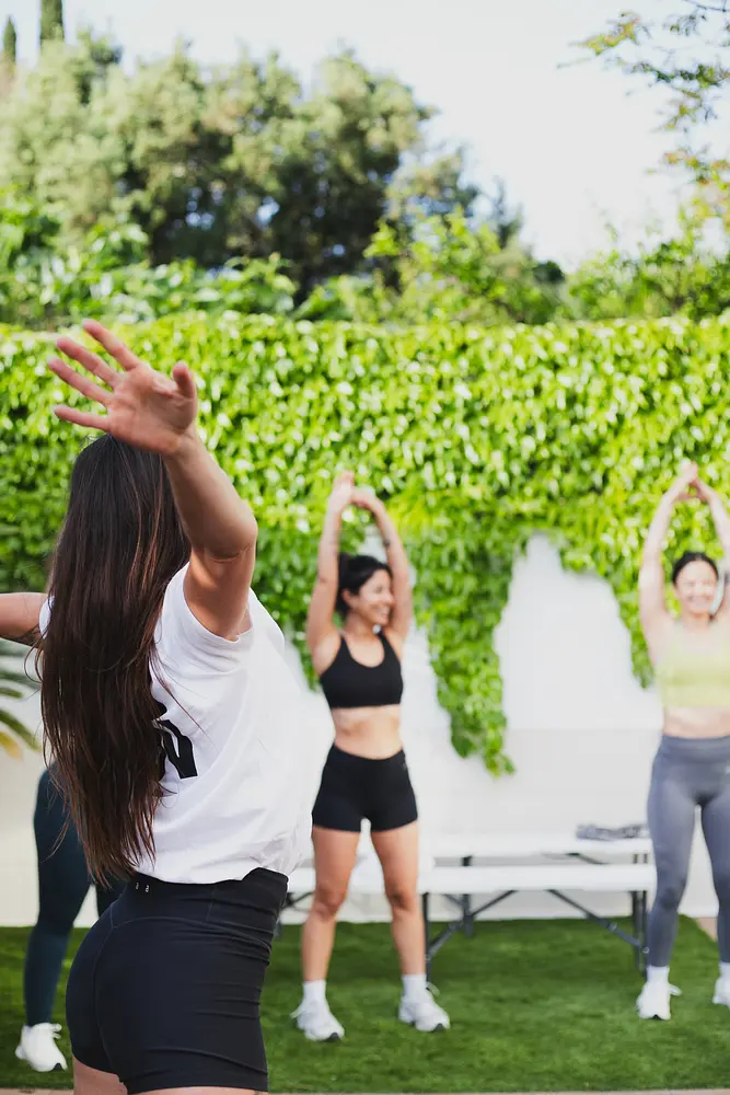 An instructor leading a group stretch exercise during an outdoor fitness class on grass